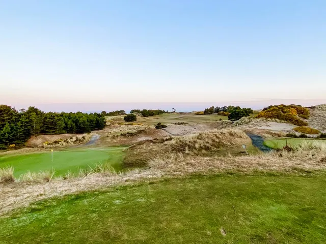 A golfer hitting a shot at Pacific Dunes, with the fairway and the ocean ahead.
