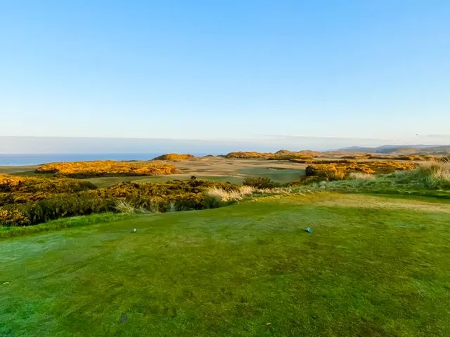 A green and flagstick at Pacific Dunes above the ocean, with a bunker short of the green.