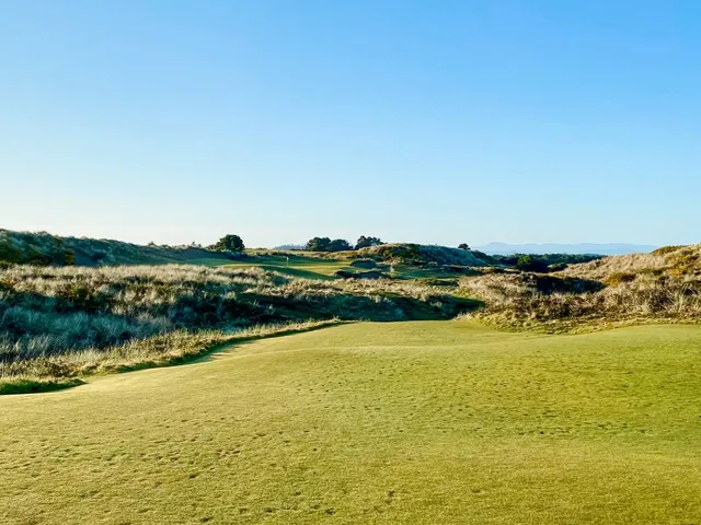 A golfer putting on a green at Pacific Dunes, with the ocean beyond the hole.