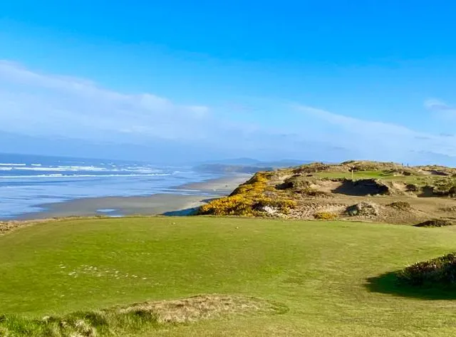 A wide fairway at Pacific Dunes, with the dunes and the Pacific in the distance.
