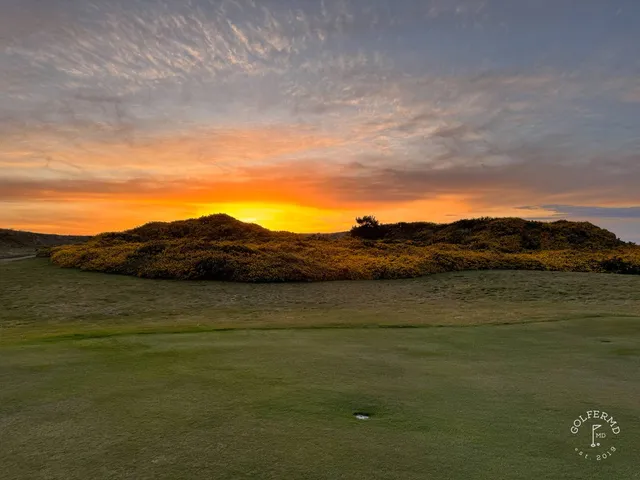 A golfer hitting a shot from the sandy rough at Pacific Dunes, with the water ahead.