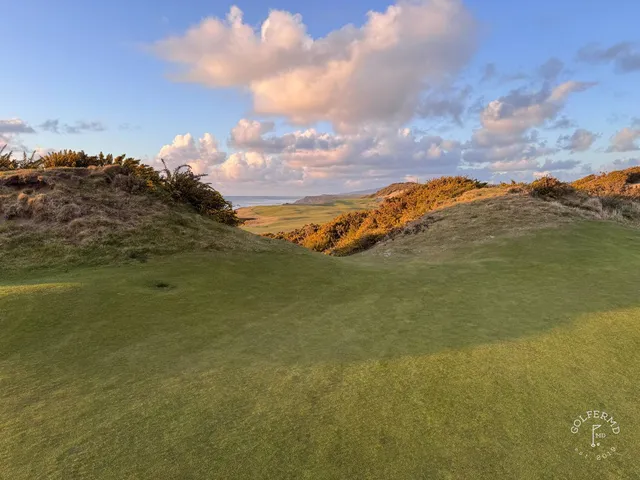 A fairway at Pacific Dunes lined with gorse, with the water in the distance.