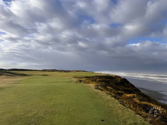 A golfer hitting a shot at Pacific Dunes, with the sandy fairway and the ocean ahead.