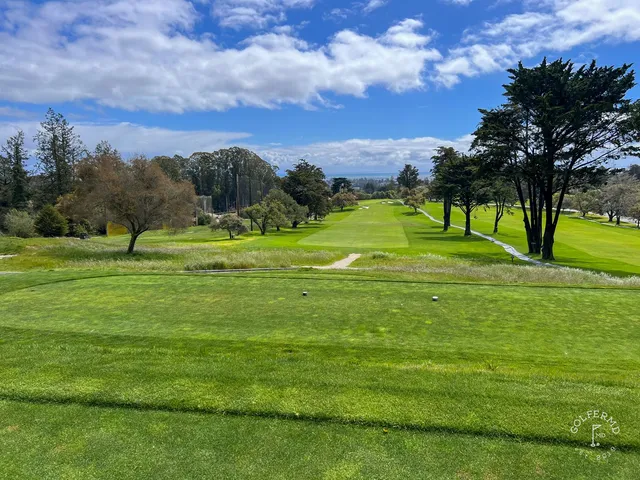 A green and flagstick at Pasatiempo Golf Club, with a bunker in front and trees behind.