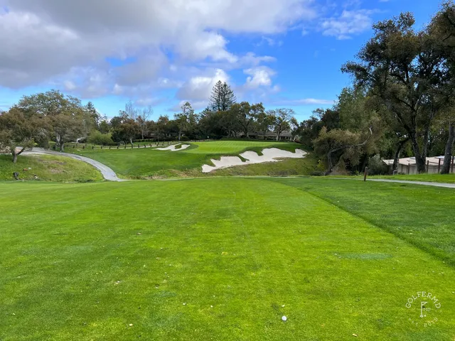 A fairway and green at Pasatiempo Golf Club, with a large tree and houses on the hill behind.