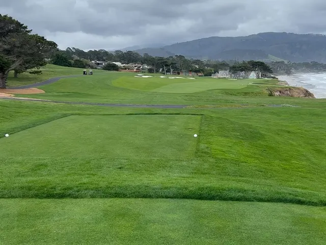 A fairway toward the ocean at Pebble Beach Golf Links, with cypress trees on the left and a bunker on the right.
