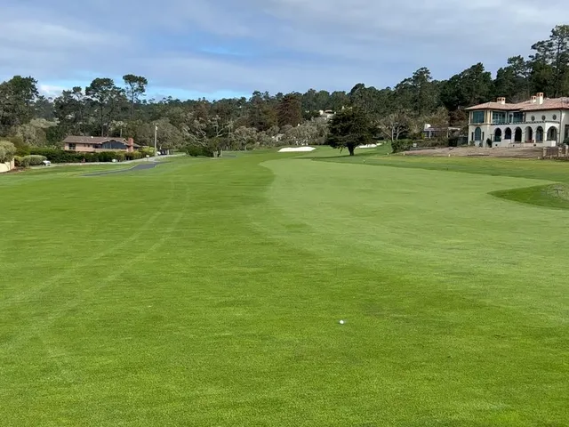 A green and flagstick above the ocean at Pebble Beach Golf Links, with the coastline curving away.