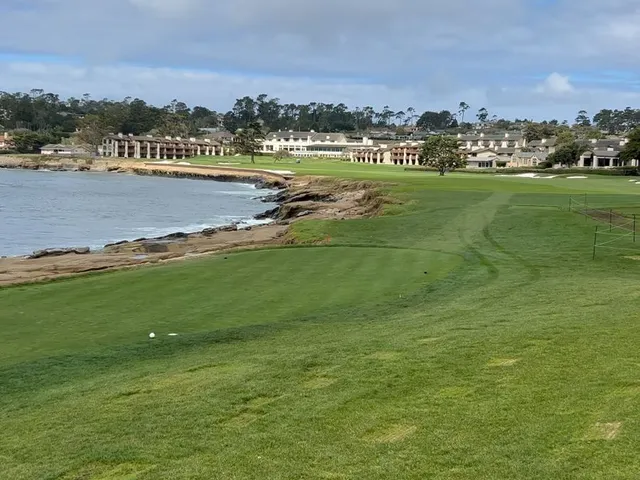 A green and flagstick on the edge of the cliff at Pebble Beach Golf Links, with cypress trees and the ocean below.