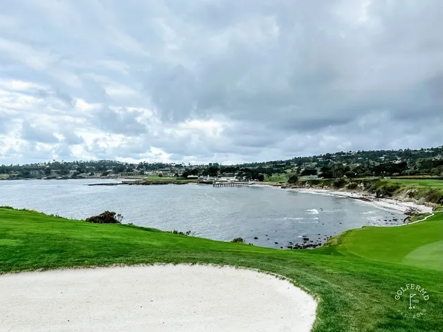 A green and flagstick beside a bunker at Pebble Beach Golf Links, with cypress trees and the ocean behind.