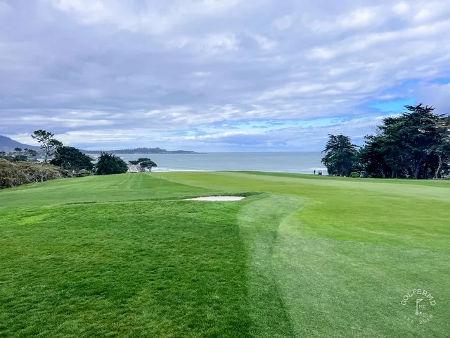 A green and flagstick framed by cypress trees at Pebble Beach Golf Links, with the ocean on the horizon.