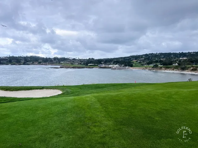 Two people walking a fairway at Pebble Beach Golf Links, with cypress trees and the ocean behind them.