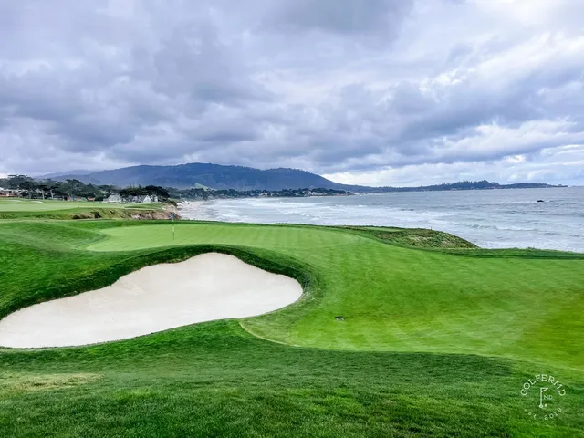 Two people walking the course at Pebble Beach Golf Links, with the ocean and cypress trees beside them.