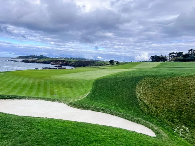 A green and fairway along the cliffs at Pebble Beach Golf Links, with the ocean and a cypress tree.