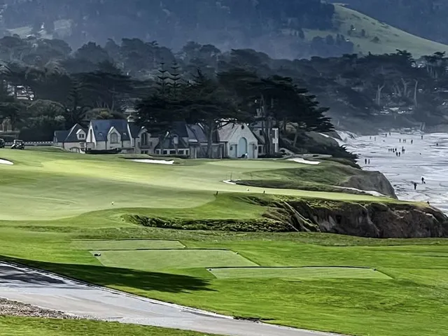 A green, flagstick, and bunker beside the ocean at Pebble Beach Golf Links, with cypress trees.