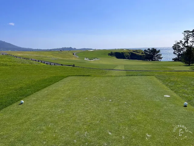A green and flagstick near the ocean at Pebble Beach Golf Links, with bunkers and cypress trees.