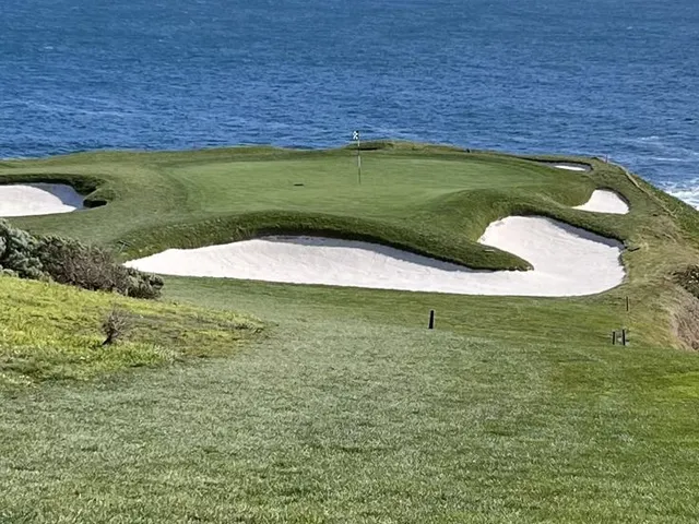 A tee shot down a narrow fairway at Pebble Beach Golf Links, with cypress trees on both sides and the ocean ahead.
