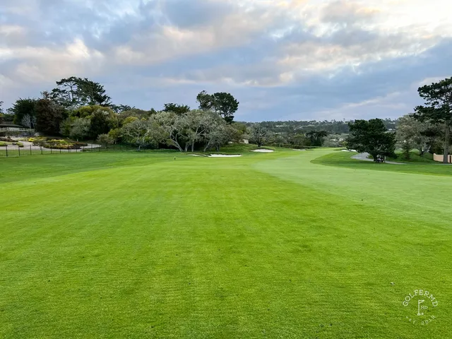 A golfer standing over a tee shot at Pebble Beach Golf Links, with the ocean and cypress trees behind the hole.