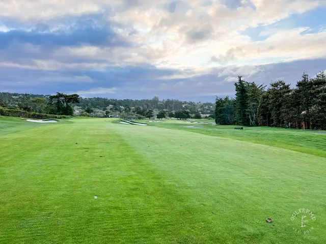 Two people on the course at Pebble Beach Golf Links, with the ocean and cypress trees behind them.