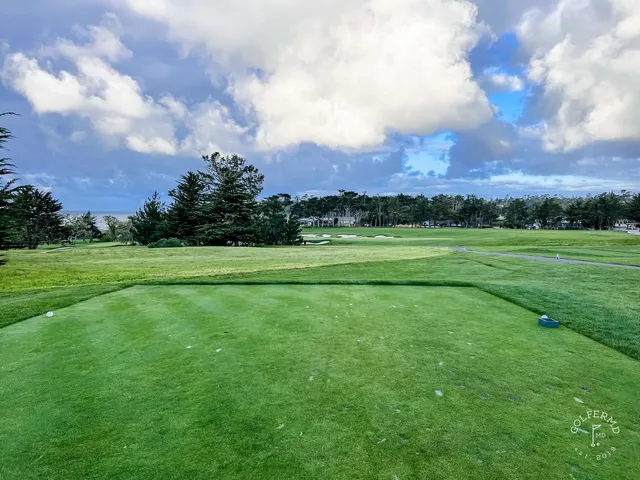 A golfer chipping toward a green at Pebble Beach Golf Links, with another person nearby and the ocean behind the shot.