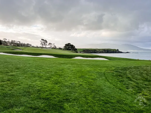 A golfer hitting a shot from the rough at Pebble Beach Golf Links, with the ocean in the background.