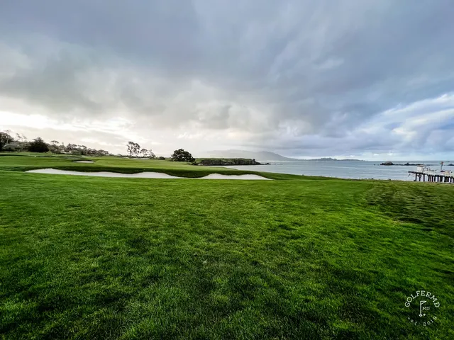 A golfer on a tee box at Pebble Beach Golf Links, with cypress trees and the ocean behind the hole.