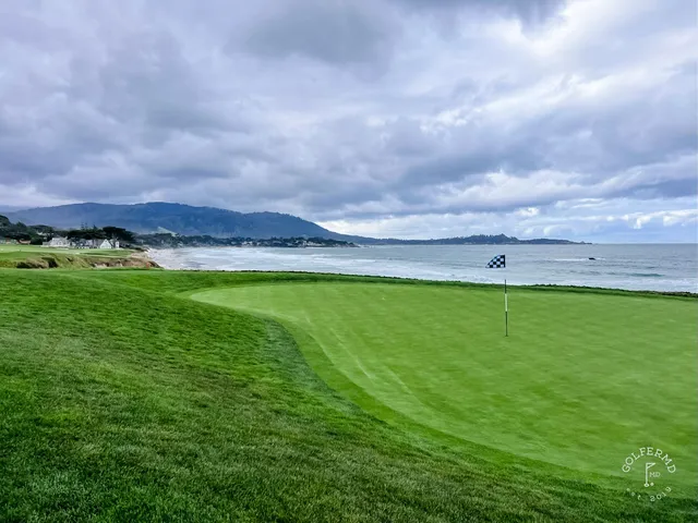 A tee shot looking down a fairway lined with cypress trees at Pebble Beach Golf Links, with a cart path along the right.