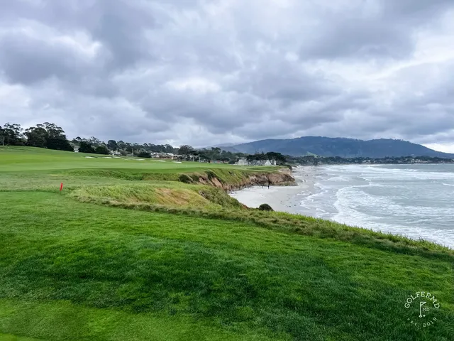 A green, flagstick, and bunker at Pebble Beach Golf Links, with two people walking nearby.