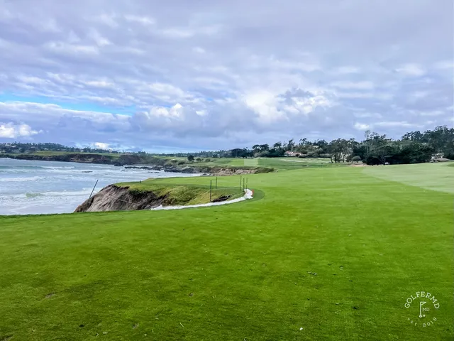Two people on a green at Pebble Beach Golf Links, with the ocean and cypress trees behind them.