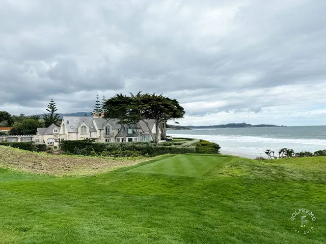 A green and flagstick above the ocean at Pebble Beach Golf Links, with a bunker in the foreground.