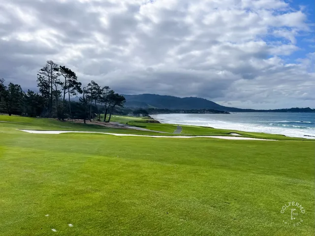 Two people beside a green at Pebble Beach Golf Links, with the ocean behind them.