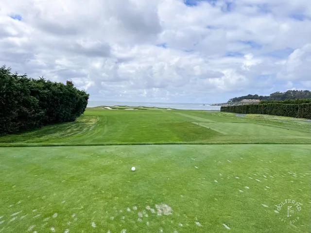 Two people walking a fairway at Pebble Beach Golf Links, with the ocean and cypress trees beside them.