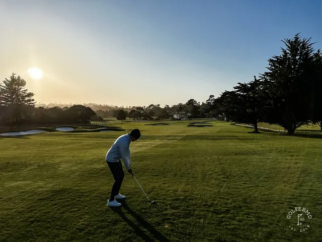 A green and bunker beside the ocean at Pebble Beach Golf Links, with cypress trees along the fairway.