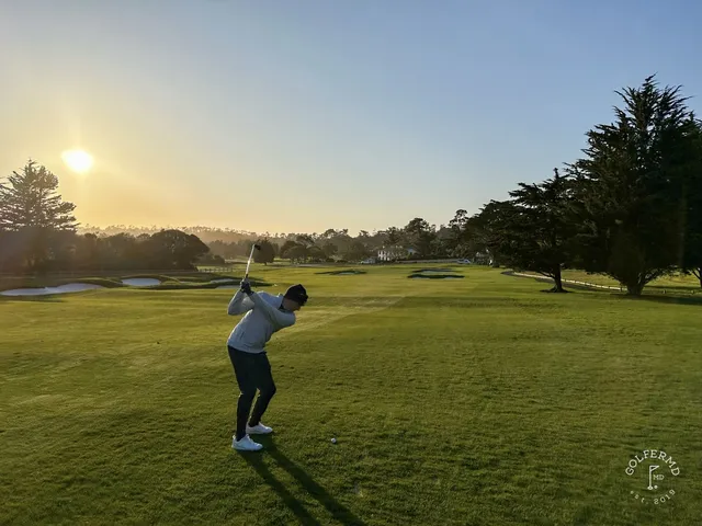 A golfer on a tee box at Pebble Beach Golf Links, with the ocean and a cypress tree behind the hole.