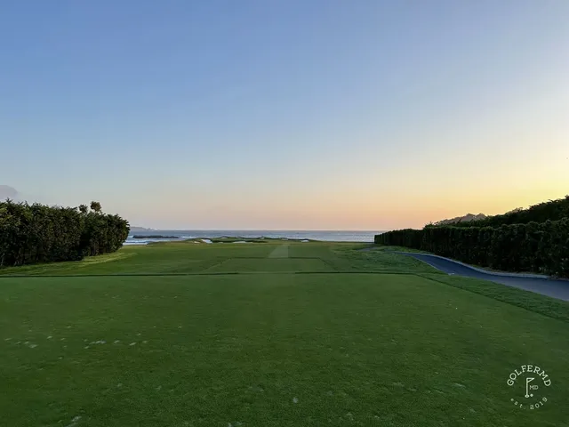 A green, flagstick, and bunker at Pebble Beach Golf Links, with the ocean and cypress trees beyond.