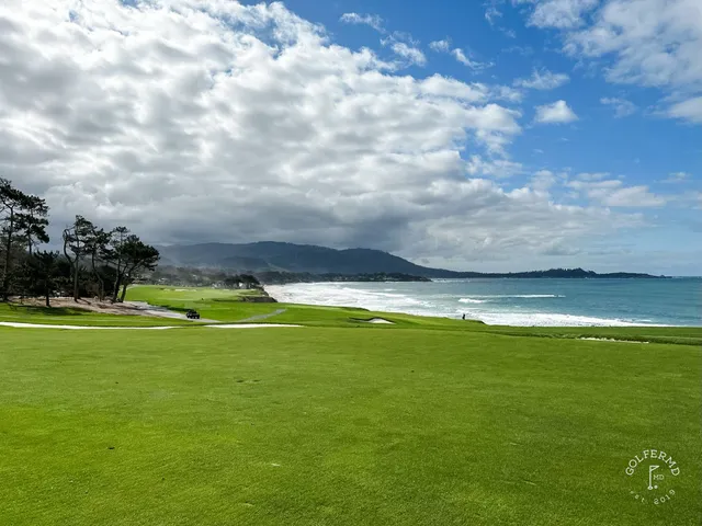 A golfer on a tee box beside the ocean at Pebble Beach Golf Links, with two other people walking the path ahead.