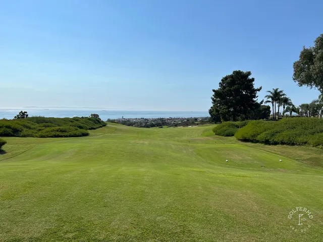 A green and flagstick above the ocean at Pelican Hill Ocean North Course, with a wide bunker in front.