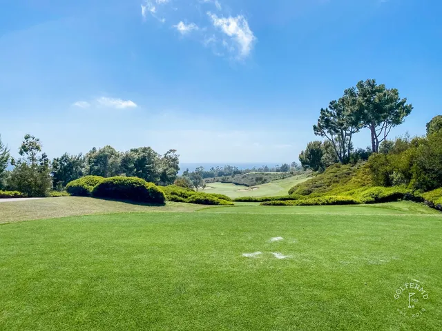 A green and flagstick above the ocean at Pelican Hill Ocean South Course, with a bunker in the foreground.
