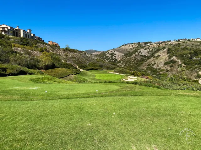A green and flagstick above the ocean at Pelican Hill Ocean South Course, with a wide bunker below the green.