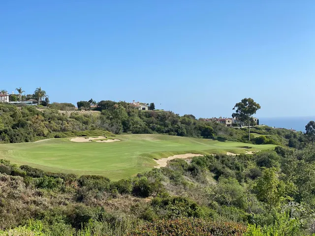 A fairway and green above the ocean at Pelican Hill Ocean South Course, with a bunker in the foreground.