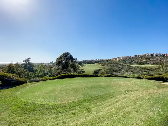 A green and flagstick above the ocean at Pelican Hill Ocean South Course, with a bunker short of the green.