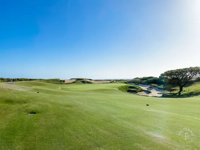 A green and flagstick above the ocean at Pelican Hill Ocean South Course, with a bunker in front of the green.