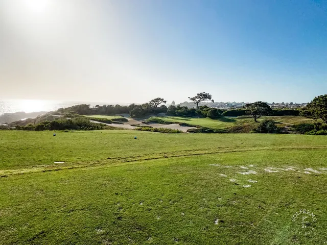A green and flagstick above the ocean at Pelican Hill Ocean South Course, with the coastline curving away.