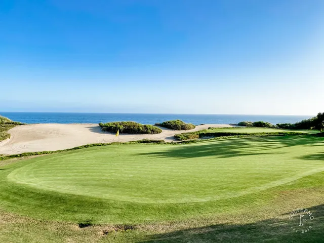 A green and flagstick above the ocean at Pelican Hill Ocean South Course, with a bunker in the foreground.