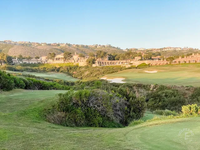 A green and flagstick above the ocean at Pelican Hill Ocean South Course, with a wide bunker in front.