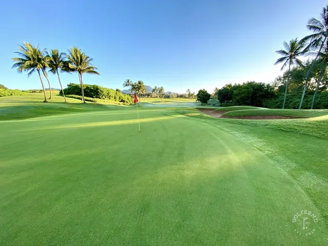 A golfer hitting a shot at Poipu Bay, with the fairway and ocean ahead.
