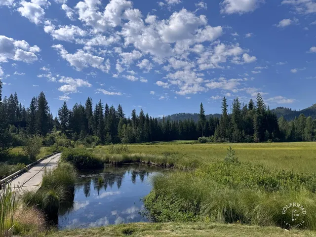 A close view of a flagstick at Priest Lake, with pines and the water behind the green.