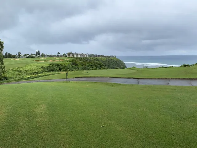 A green and flagstick at Princeville Makai, with the ocean and a rocky coast behind the hole.