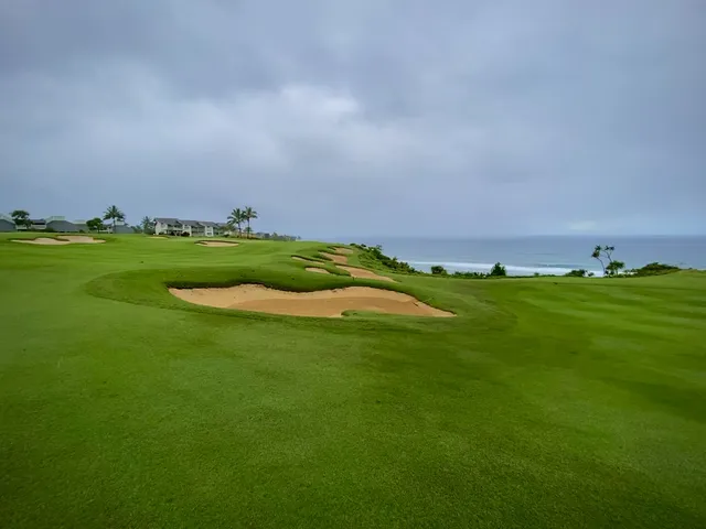 A golfer hitting a shot at Princeville Makai, with the ocean and mountains behind the hole.
