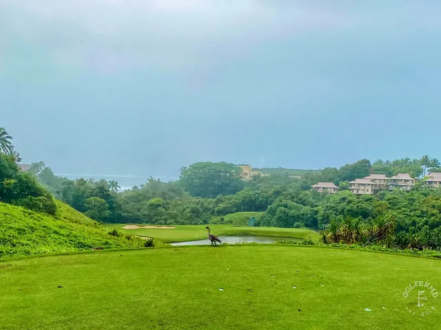A green and flagstick at Princeville Makai, with a sand bunker in front and the ocean behind the hole.