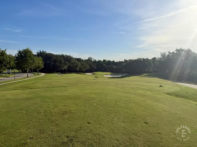 A green and flagstick at the Palmer Course, with a pond in front and a sand bunker behind the green.
